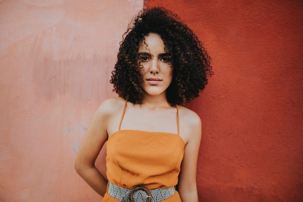 Woman wearing an orange top standing beside pink wall