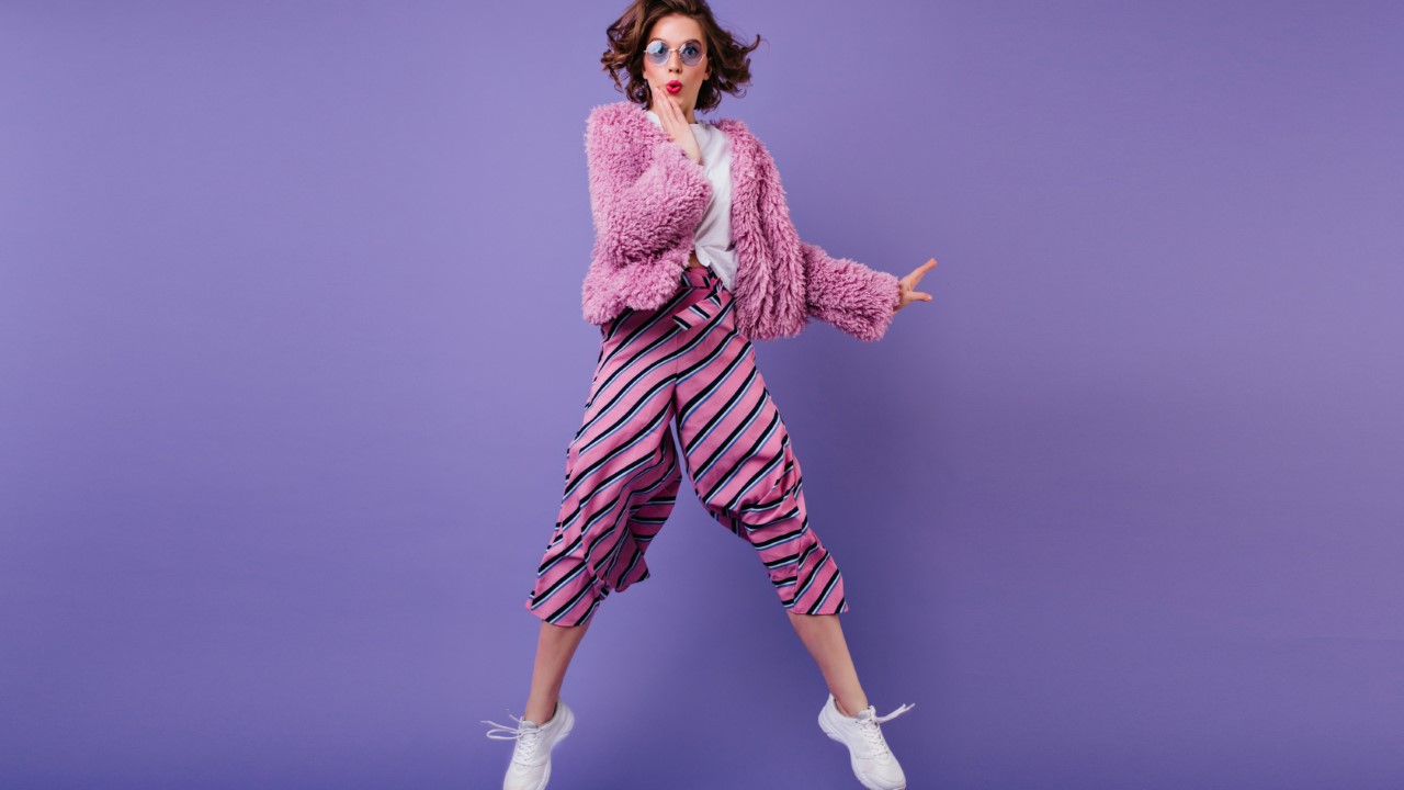 Full-length shot of glad curly woman in striped pants jumping on